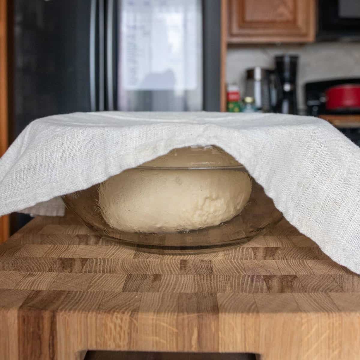 dough ball in a glass mixing bowl covered with a paper towel