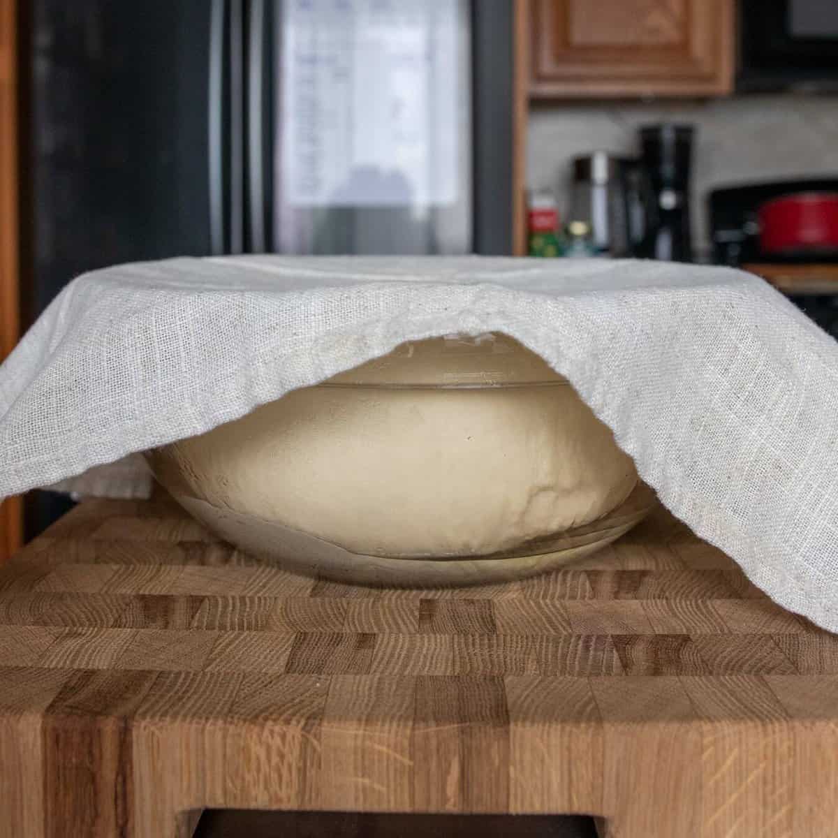 dough ball in a glass mixing bowl covered with a paper towel after rising