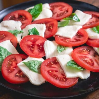 platter of caprese salad with fresh sliced tomatoes, fresh basil and sliced mozzarella