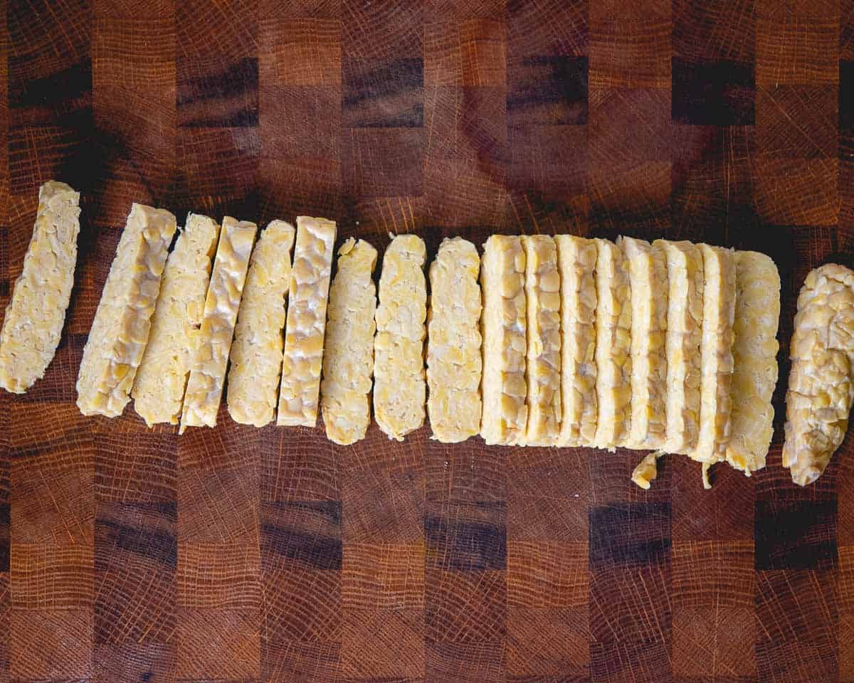sliced, uncooked tempeh lined up on a wooden cutting board