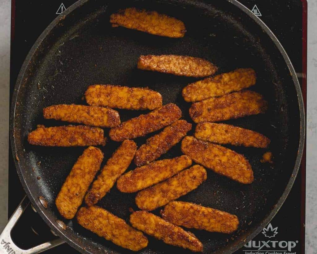 overhead shot of tempeh bacon cooking in the pan, almost finished