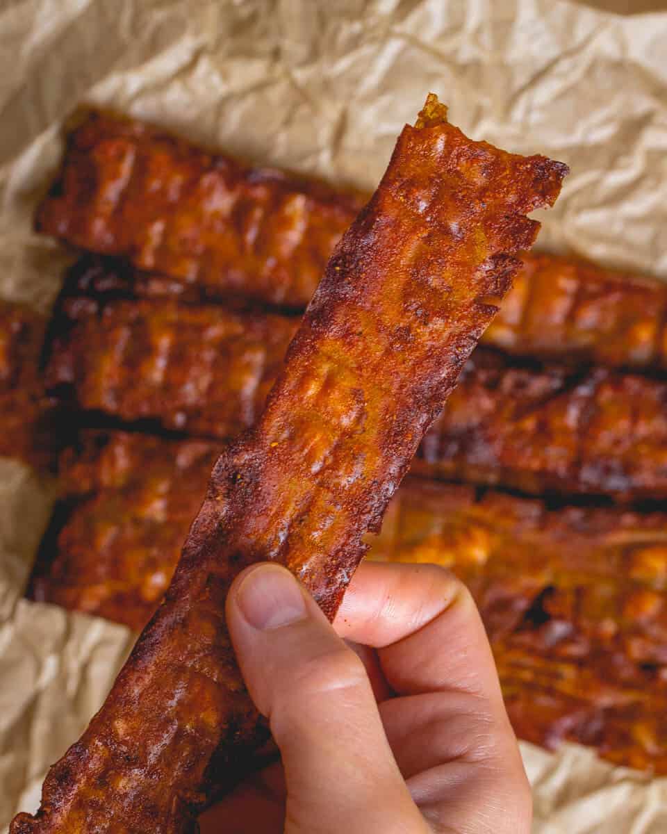 closeup shot of author holding slice of gordon ramsay's vegan bacon