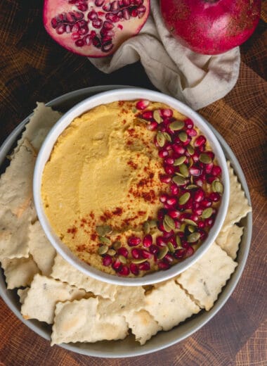 Overhead shot of pumpkin hummus topped with pomegranate seeds and served with rosemary crackers.