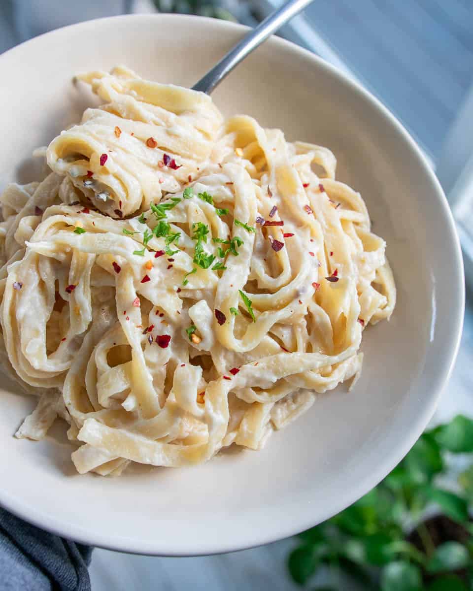 vegan fettuccine alfredo in a bowl topped with fresh parsley and red pepper flakes
