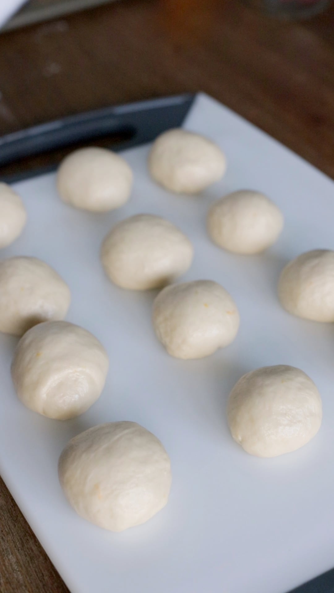 12 balls of dough resting on a plastic cutting board