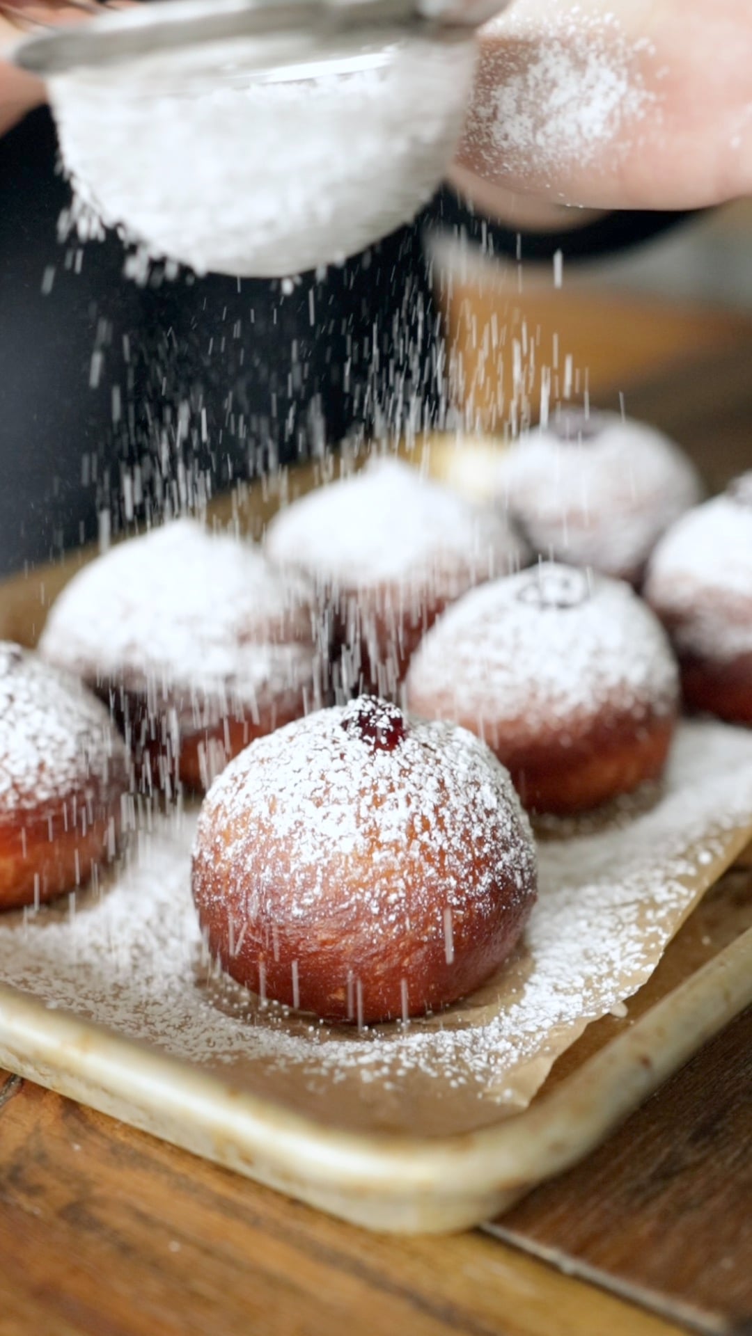 a plate of vegan sufganiyot being dusted with powdered sugar