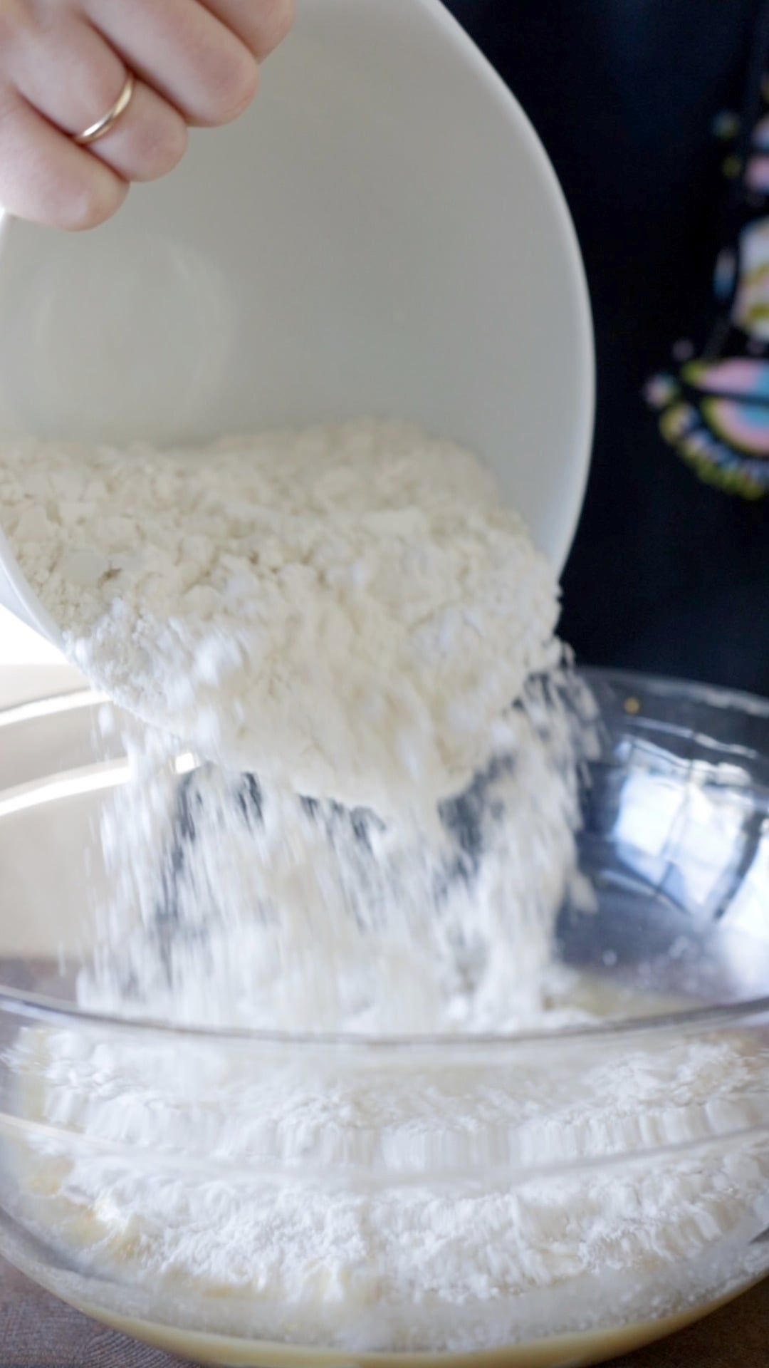flour being poured into a large glass mixing bowl