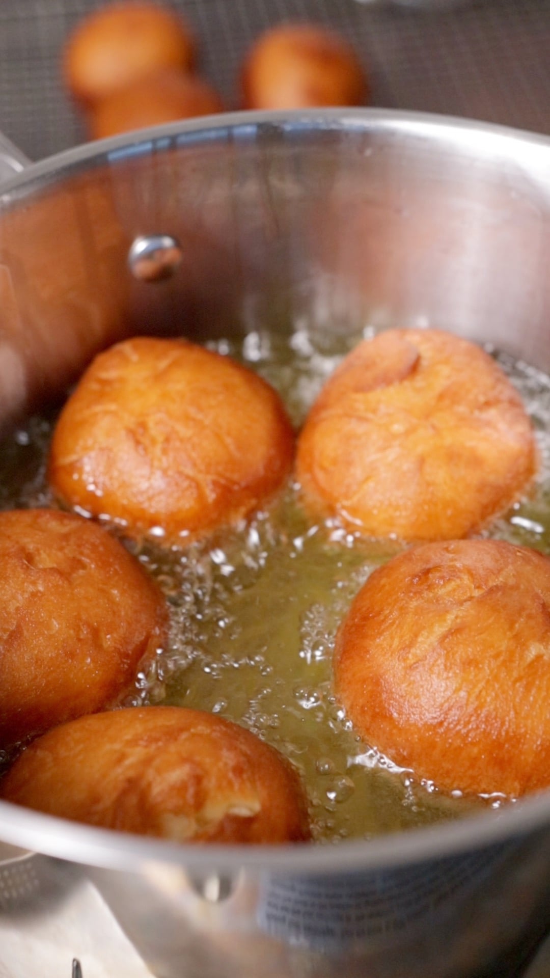 5 balls of dough being deep fried in oil