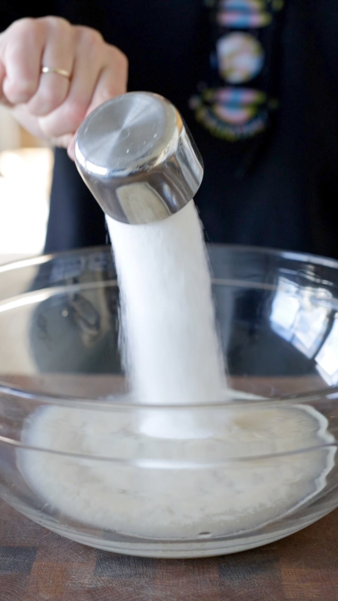 sugar being poured into a large glass mixing bowl