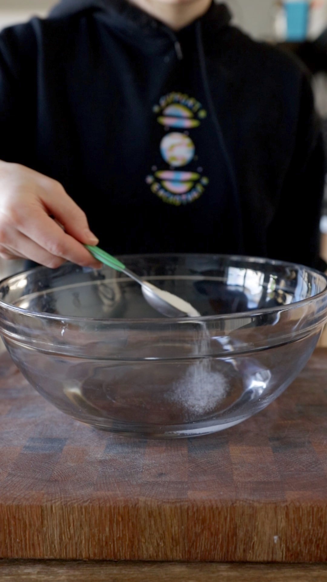 sugar being sprinkled into a large glass mixing bowl