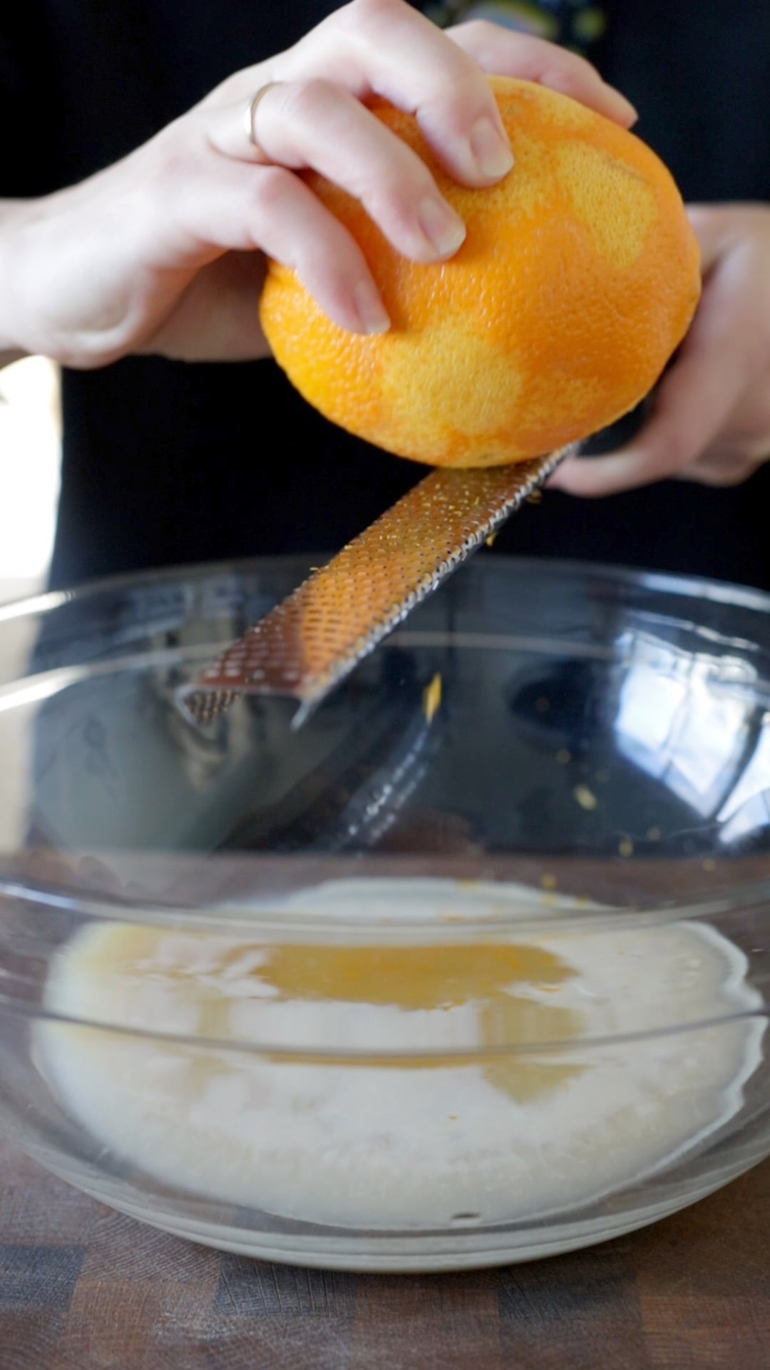 an orange being zested into a large glass mixing bowl