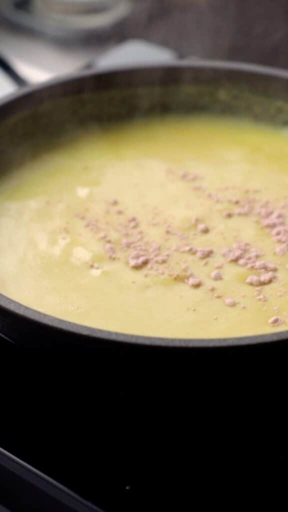black salt being added to the vegan yolk sauce in a small saucepan