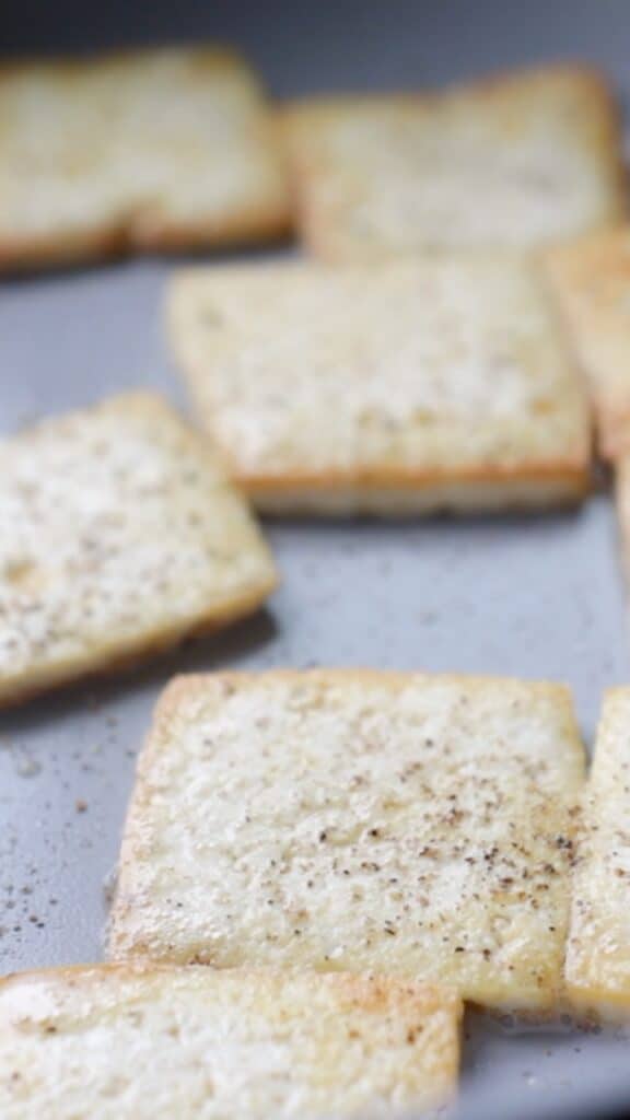 sliced tofu being pan-fried in a small skillet