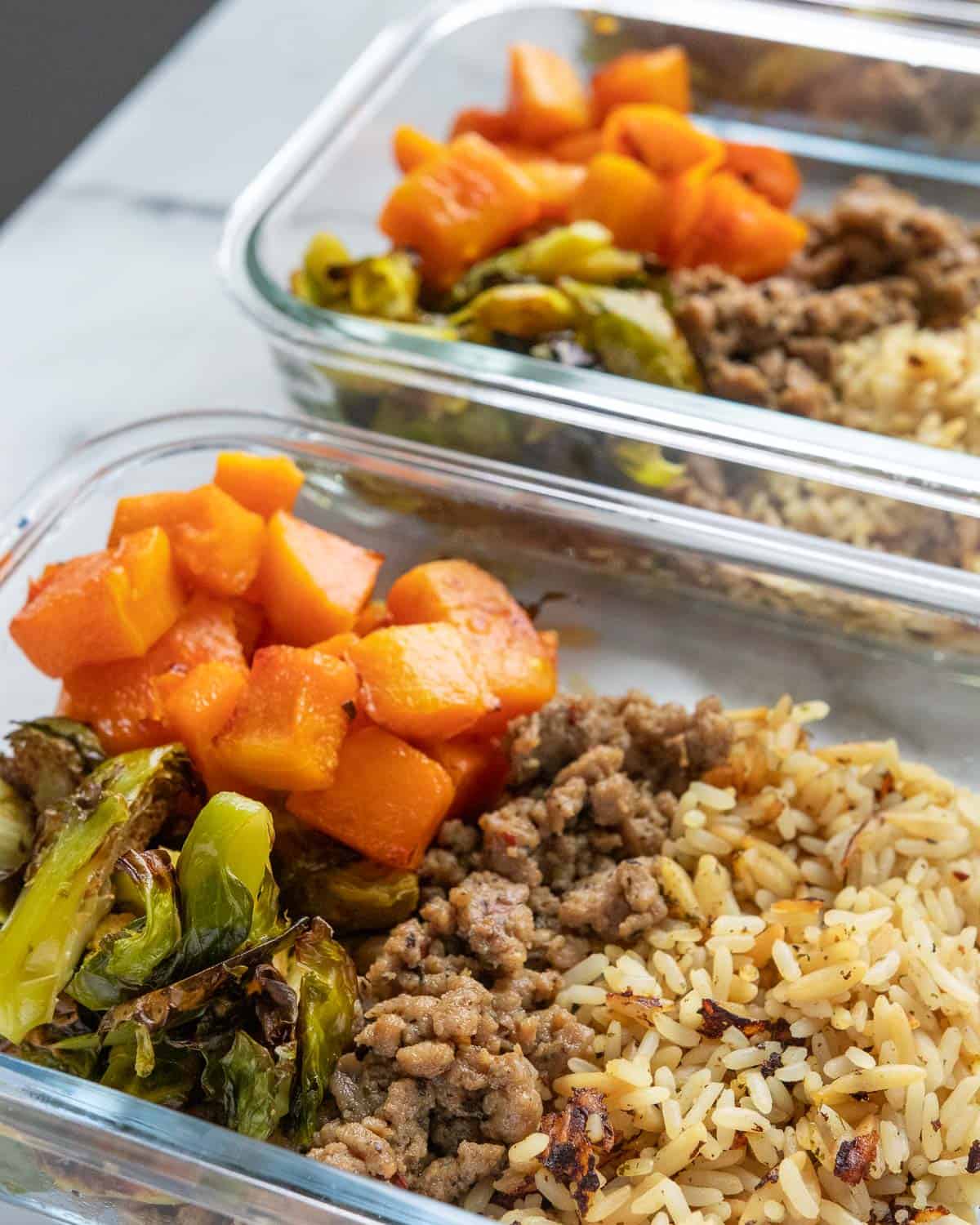 closeup up meal prep container with roasted squash and brussels sprouts, sausage, and rice pilaf