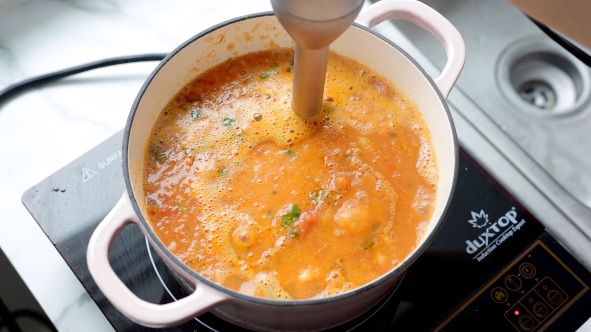 a pot of vegan tomato soup being immersion blended