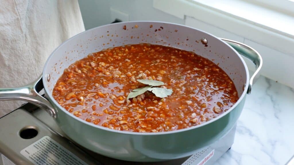 tofu bolognese simmering in a pan with three bay leaves sitting on top