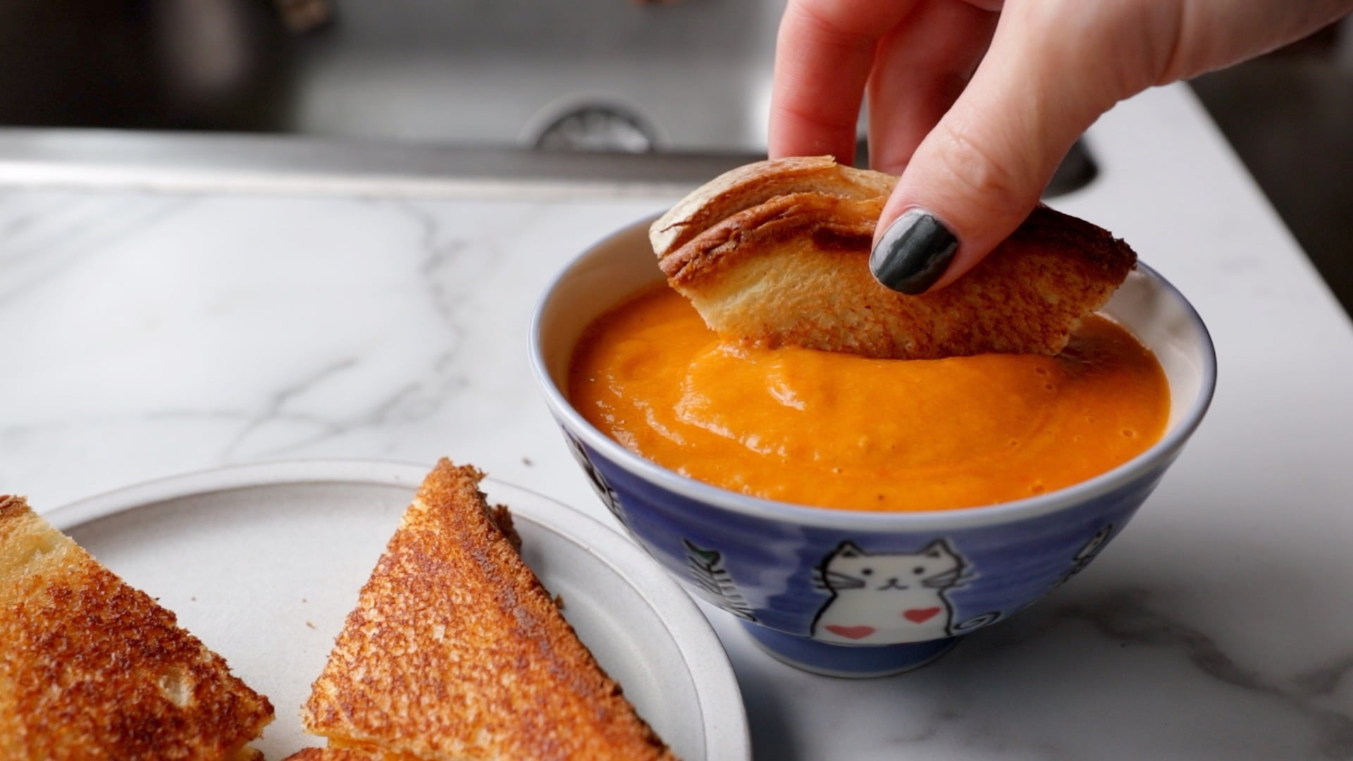 a triangular piece of a vegan grilled cheese being dipped into tomato soup