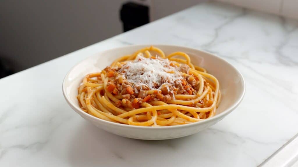 finished tofu bolognese and bucatini with a pile of freshly grated vegan parmesan cheese on top