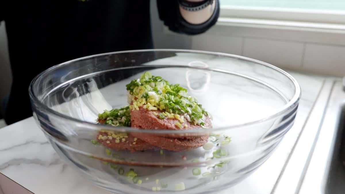 minced scallions, garlic, and ginger sitting atop four raw Impossible patties in a large glass mixing bowl