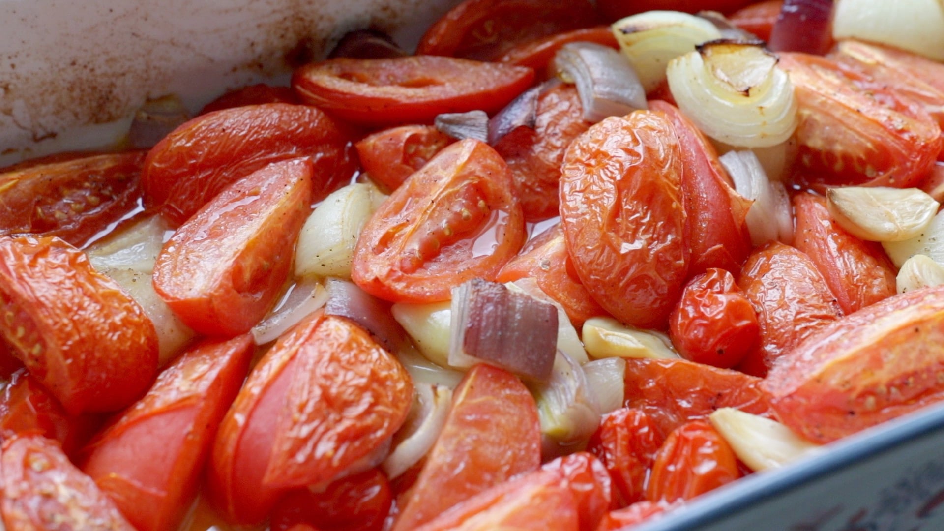tomatoes, red onion, and garlic tossed with olive oil in a baking dish after roasting