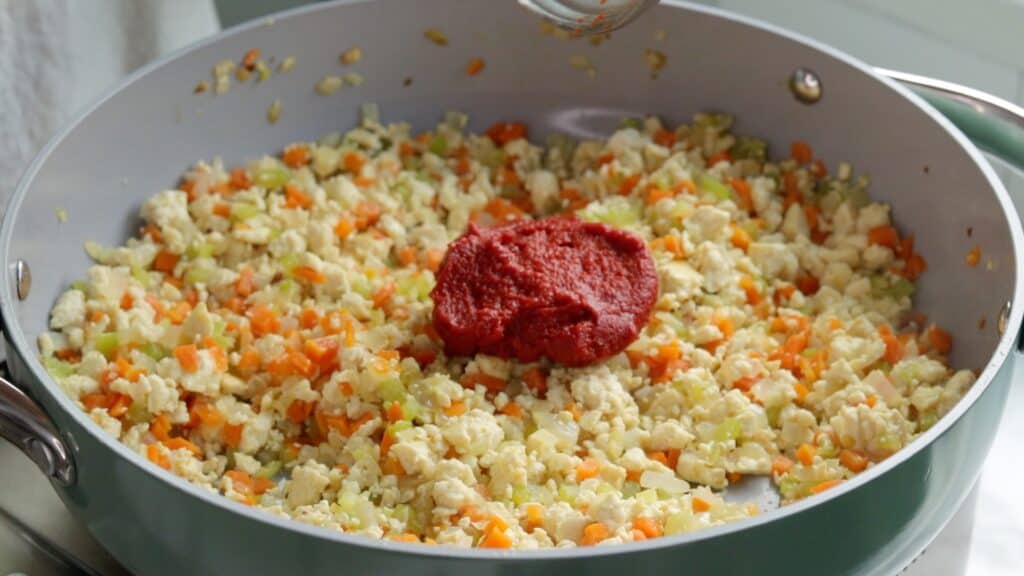 a dollop of tomato paste sitting atop a mixture of crumbled tofu and sautéed carrot, onion, and celery