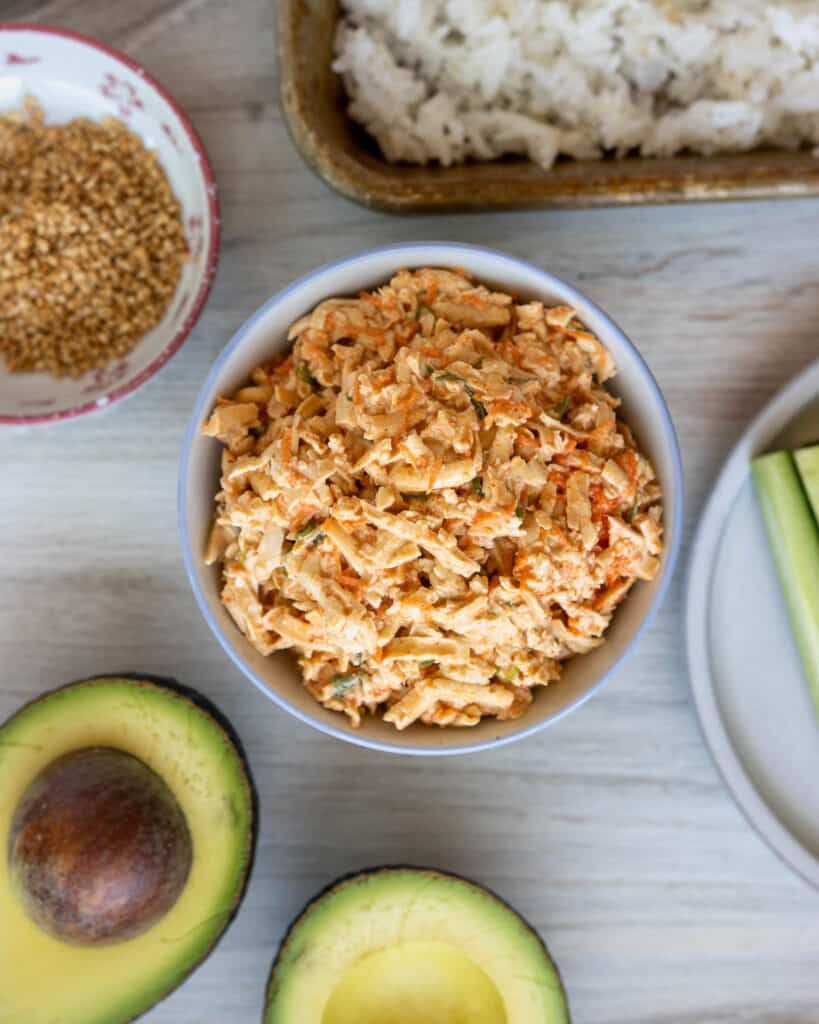 An overhead view of a bowl of spicy tuna salad, surrounded by prepped ingredients for vegan California rolls.