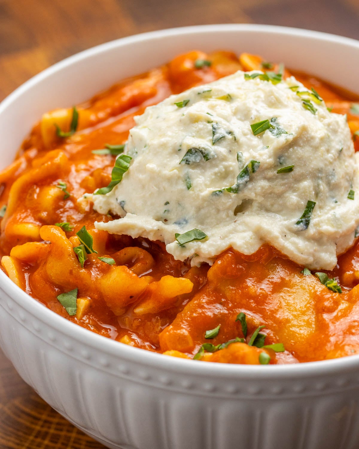 A close-up shot of vegan lasagna soup, with a big dollop of vegan herbed ricotta on top. It is topped with chopped fresh basil.
