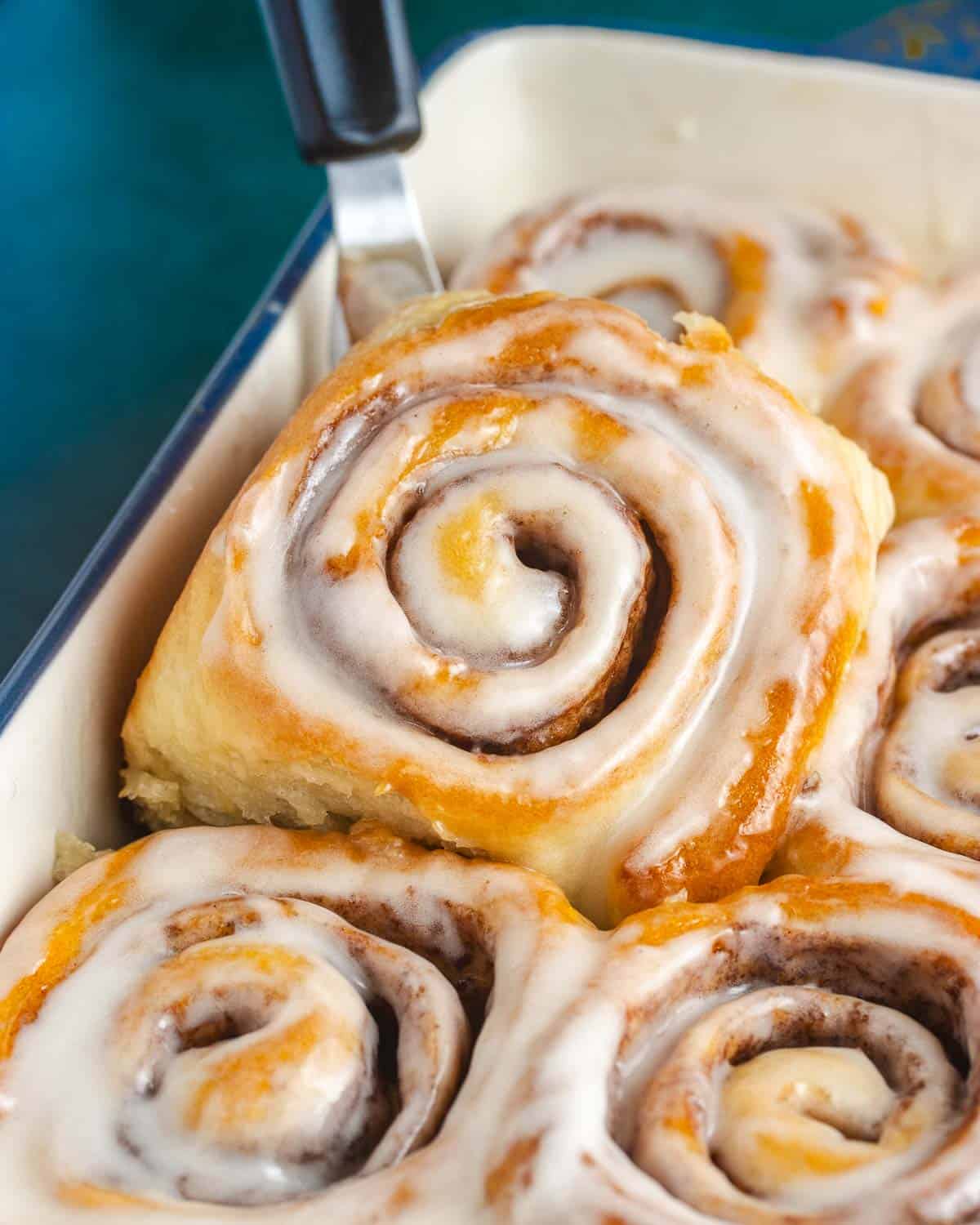 close up of a vegan cinnamon roll being lifted out of a baking pan
