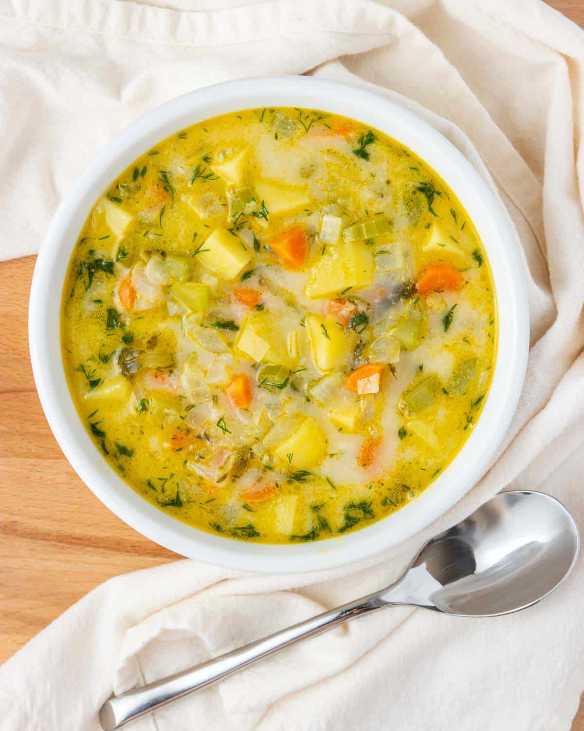 overhead shot of a bowl of vegan pickle soup, with a kitchen towel and a spoon beside it
