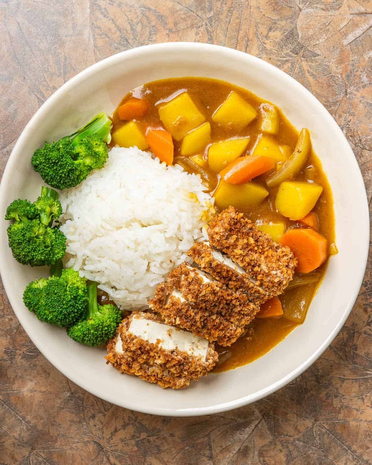 a large white bowl filled with vegan Japanese curry, crispy tofu katsu, white rice, and steamed broccoli