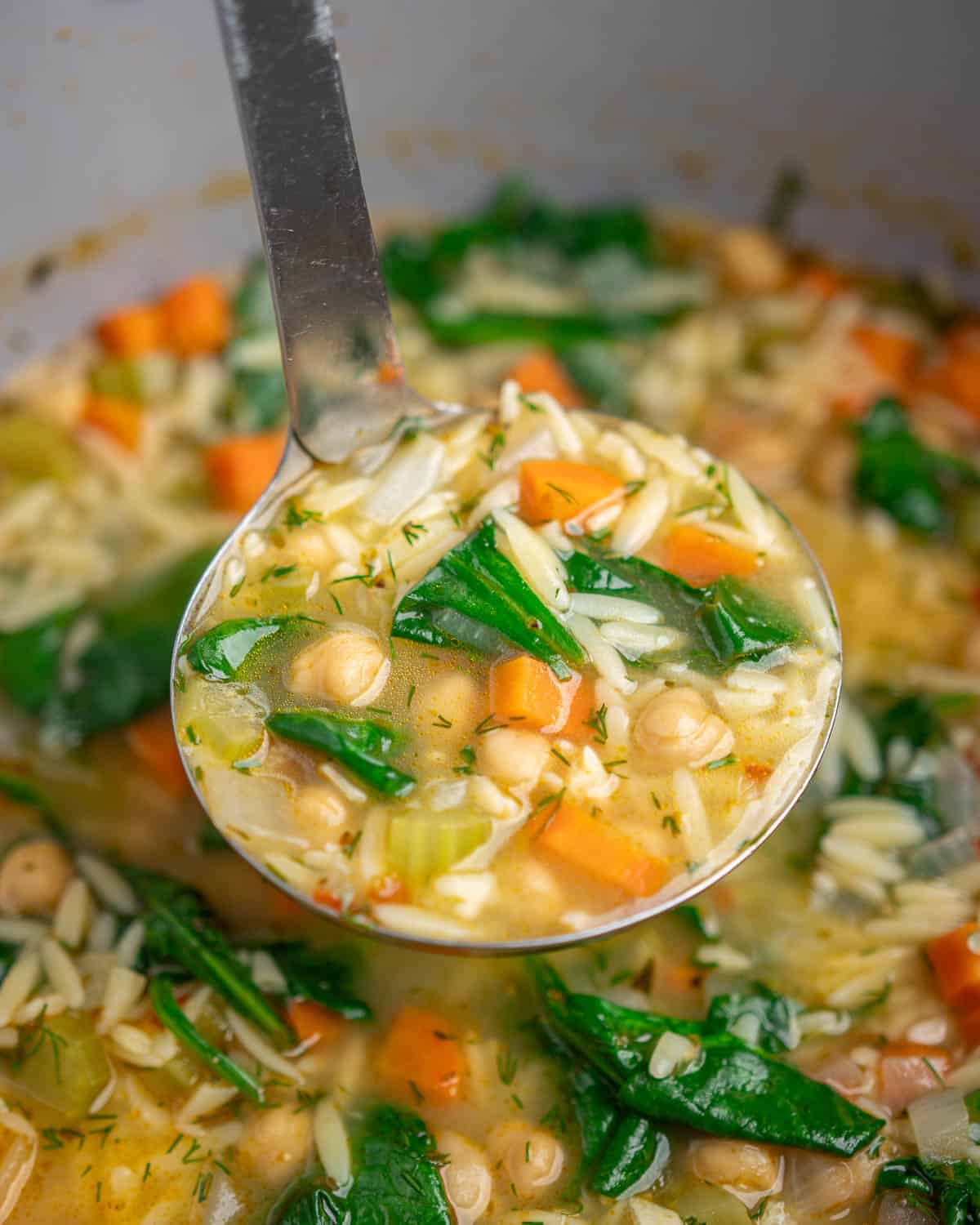 close-up of a ladle full of lemon chickpea orzo soup