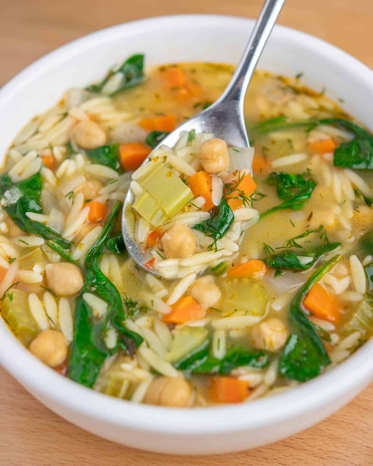 a bowl of lemon chickpea orzo soup, with a spoonful of soup