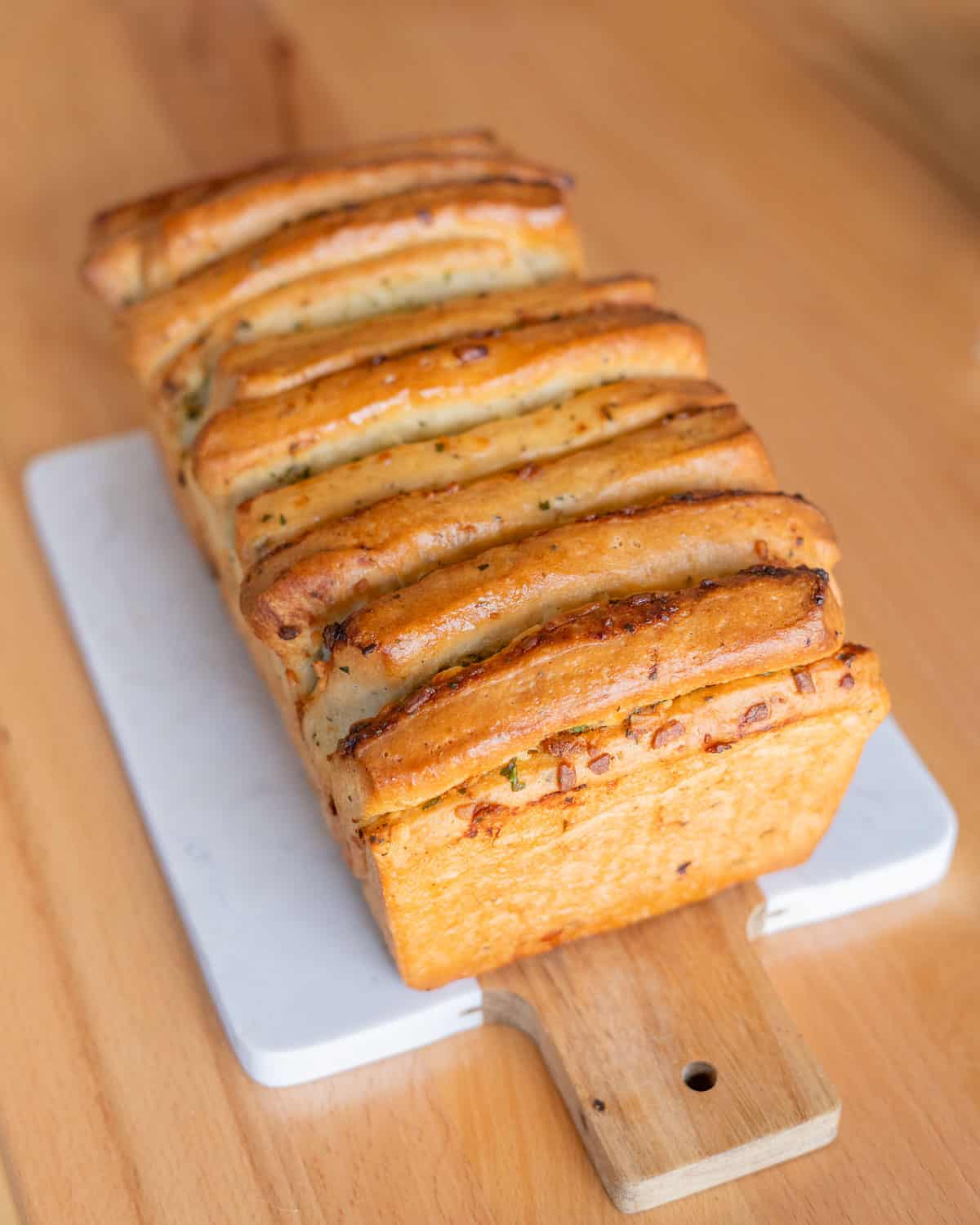 a loaf of garlic herb pull-apart bread on a wood and marble cutting board
