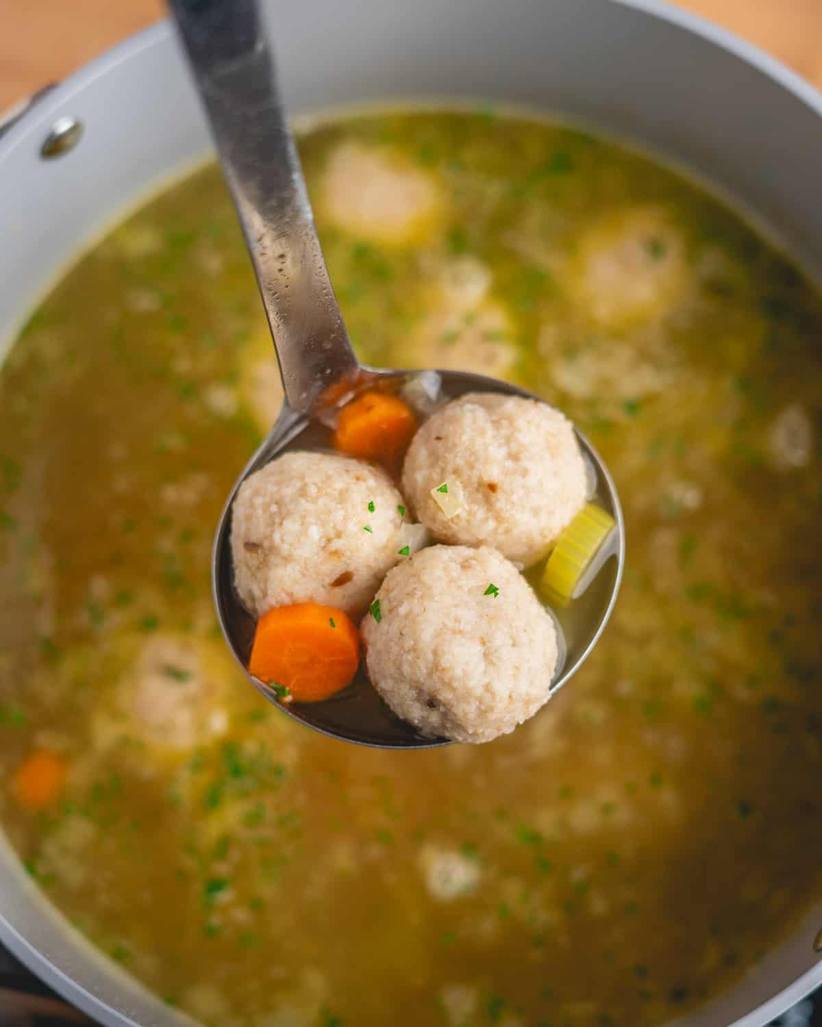 a ladle full of three vegan matzo balls, some broth, two pieces of carrot, and a piece of celery