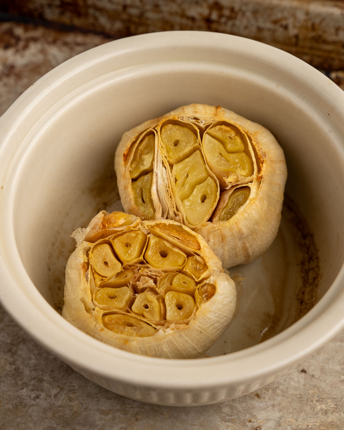 2 heads of roasted garlic with the tops sliced off in a ramekin and topped with olive oil and salt