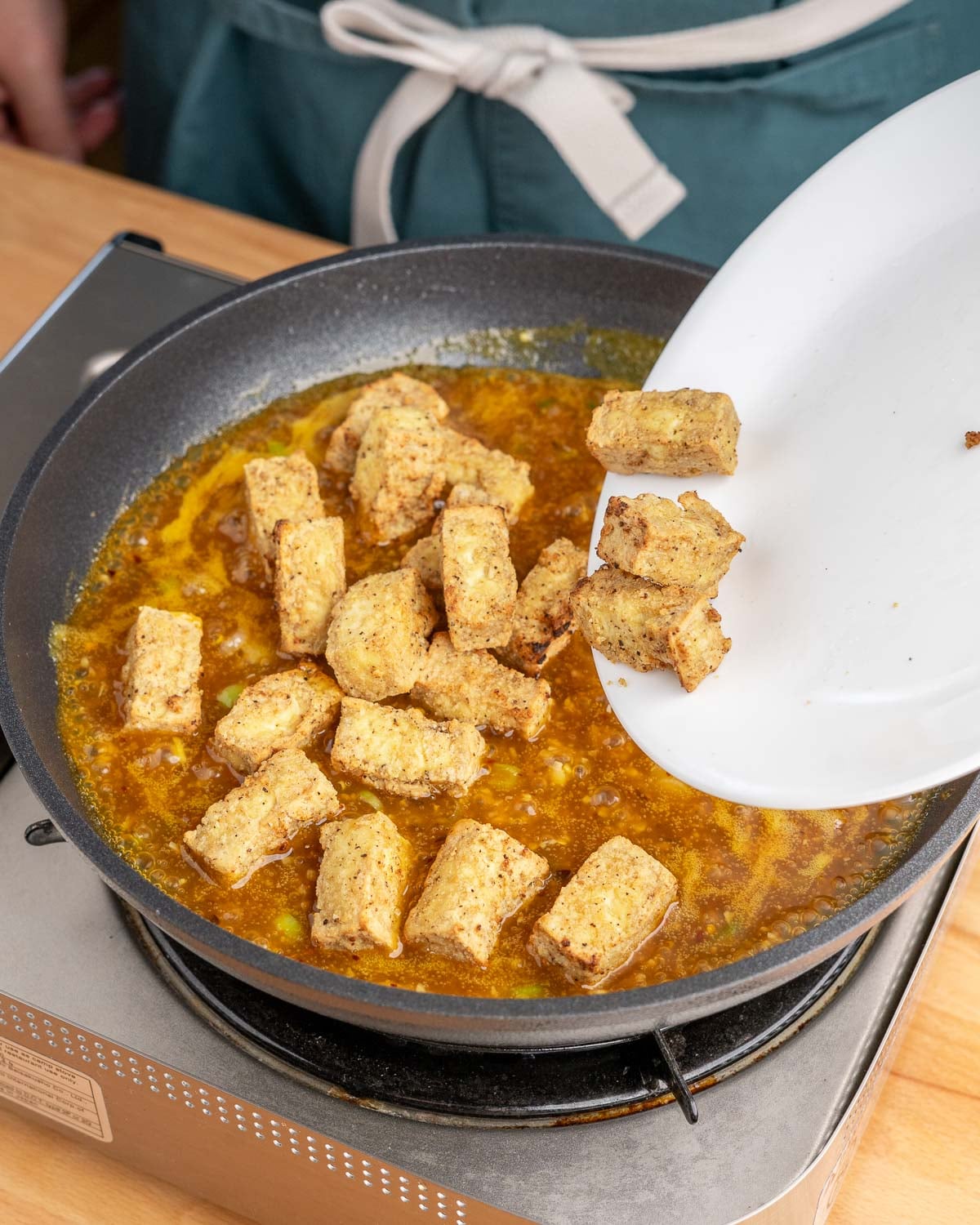 Adding crispy air fryer tofu to orange sauce in the pan.