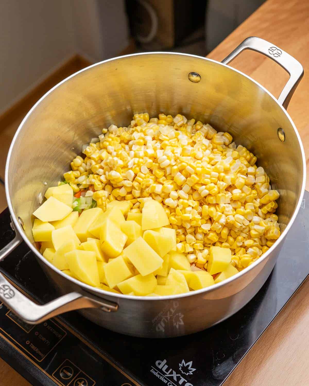 Potatoes and corn added to soup pot.