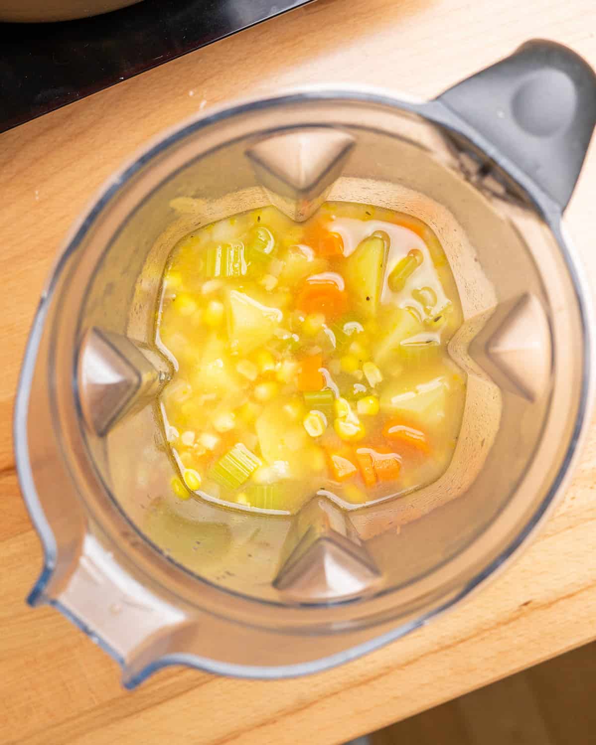Overhead shot of blender with a few cups of corn chowder removed to blend and thicken the soup.