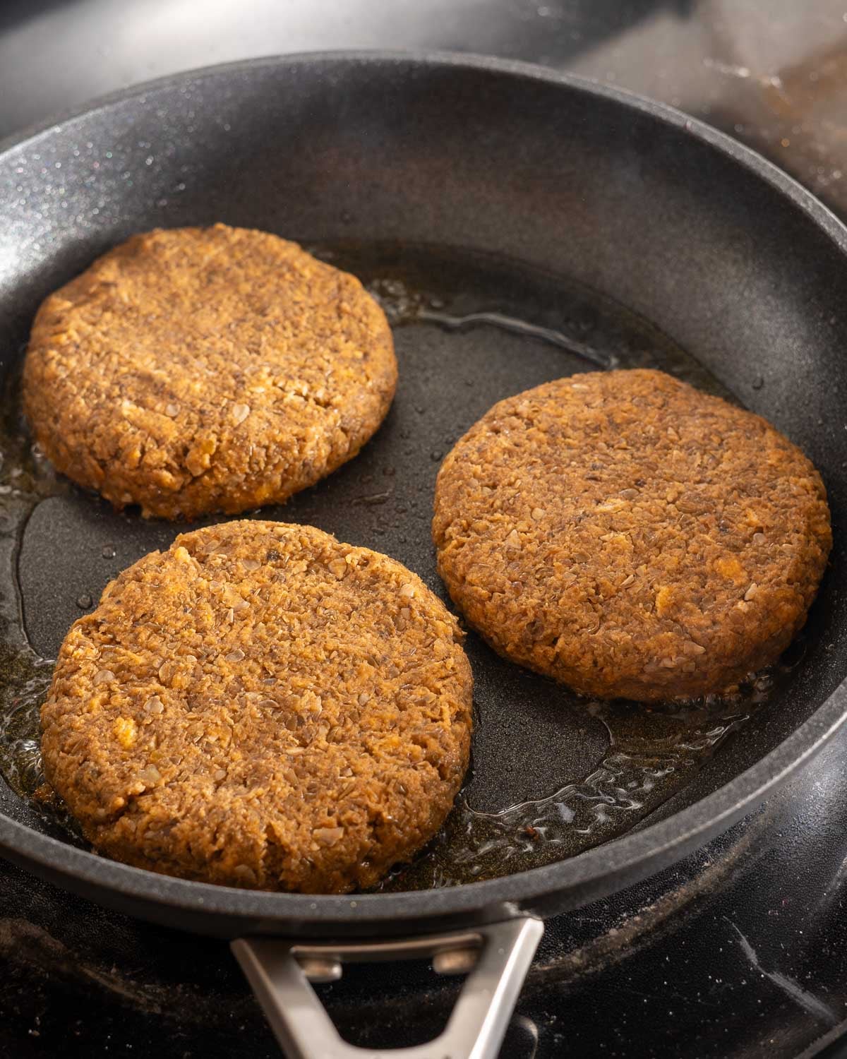 Lentil burgers frying in a skillet.