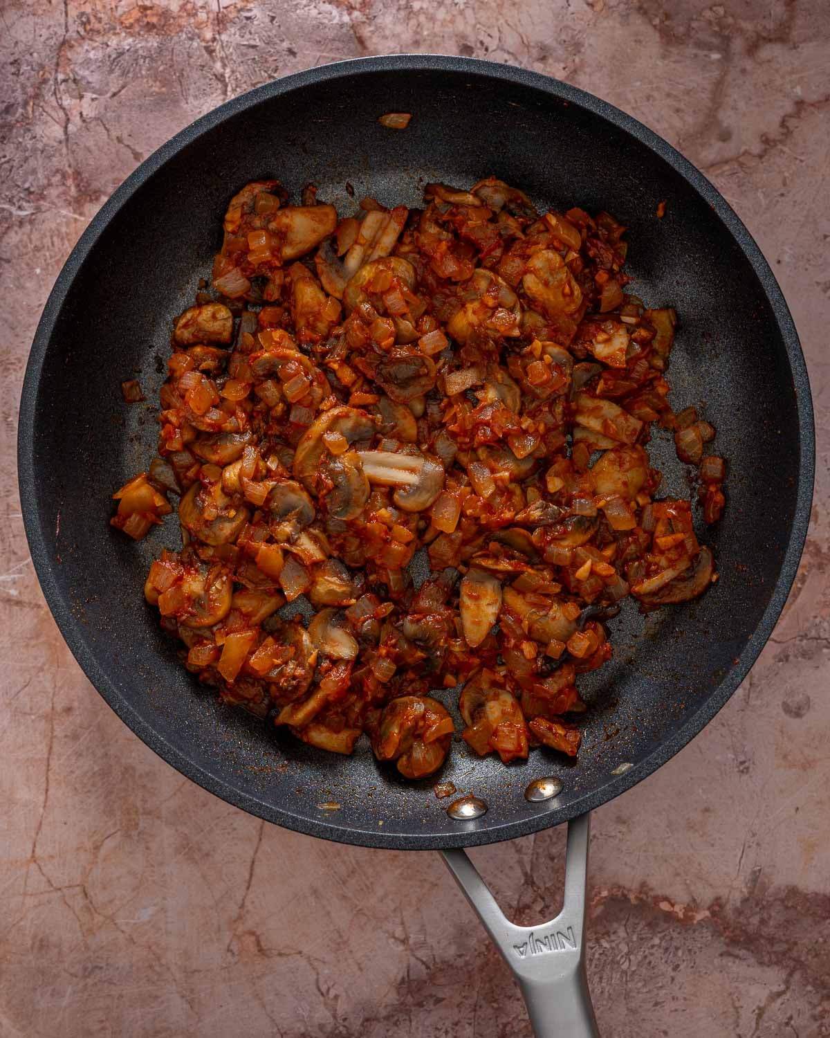 Sautéed mushrooms, onion and garlic with tomato paste in a skillet.