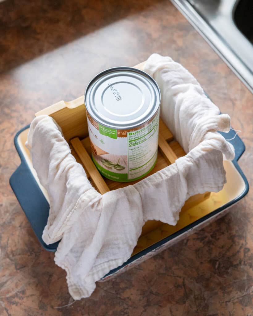 Tofu in mold weighed down with a can to press out extra liquid