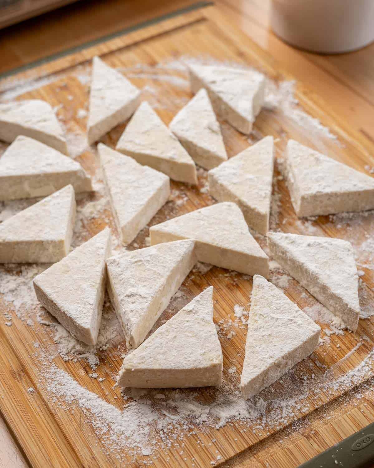 triangular pieces of tofu, dusted with flour, on a wooden cutting board