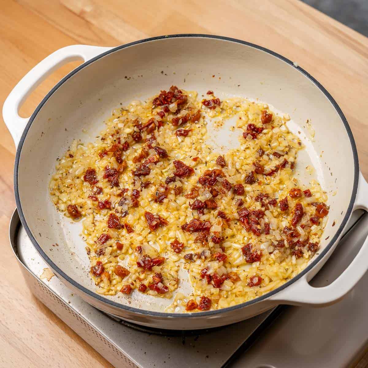 diced onion, red pepper flakes, and chopped sun-dried tomatoes sautéing in a braiser pan
