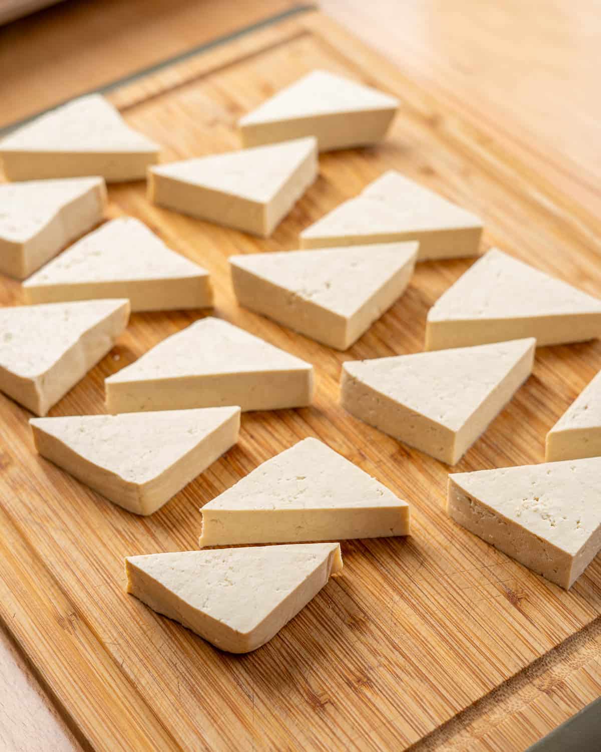 triangular pieces of tofu on a wooden cutting board