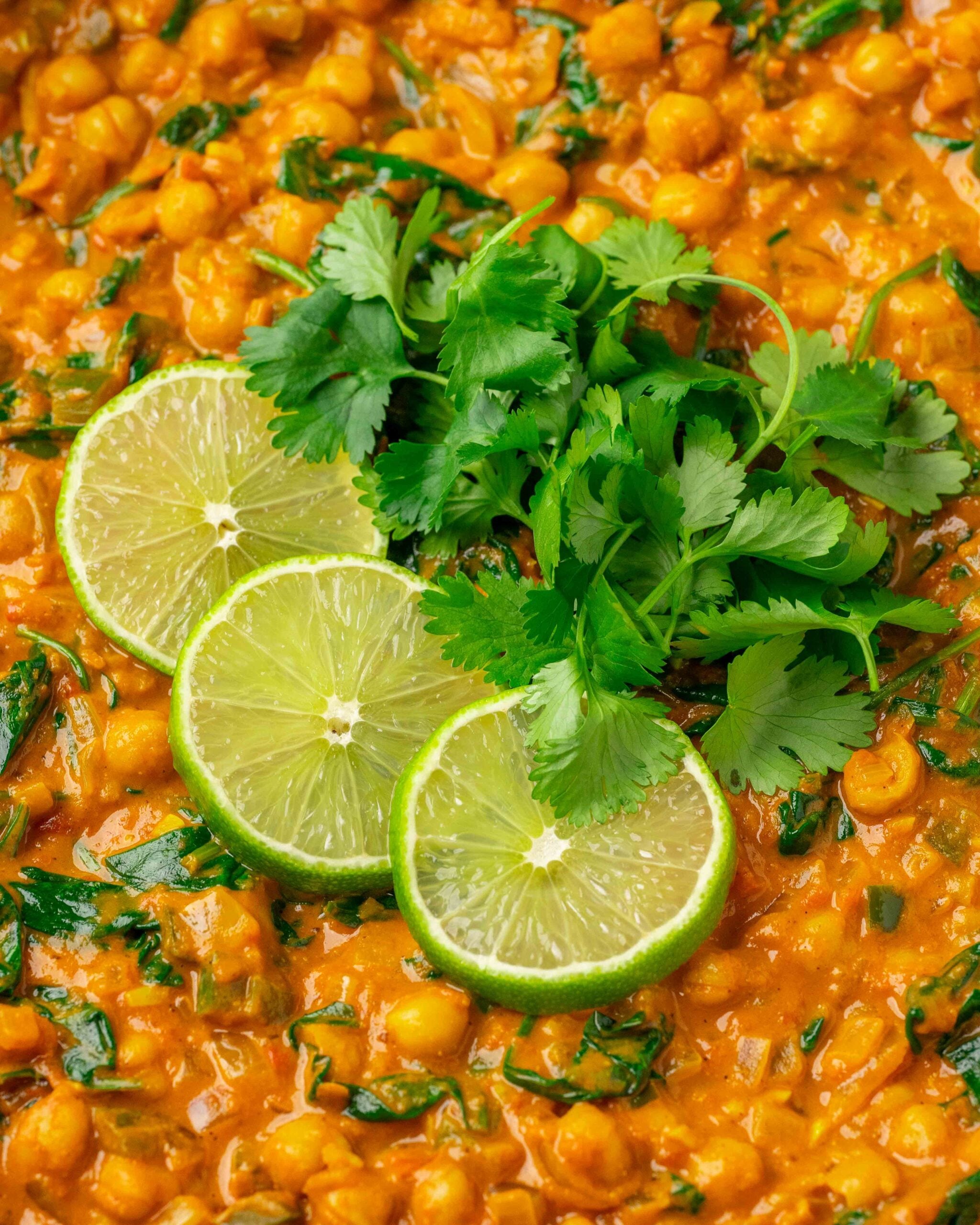 close up of chickpea curry garnished with cilantro and slices of lime