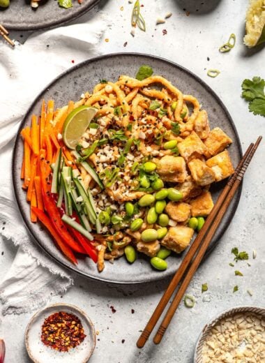 overhead shot of vegan peanut noodles topped with tofu, edamame, carrot, cucumber, scallion, and a lime wedge