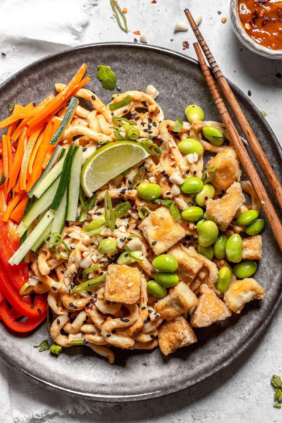 overhead shot of vegan peanut noodles topped with tofu, edamame, carrot, cucumber, scallion, and a lime wedge
