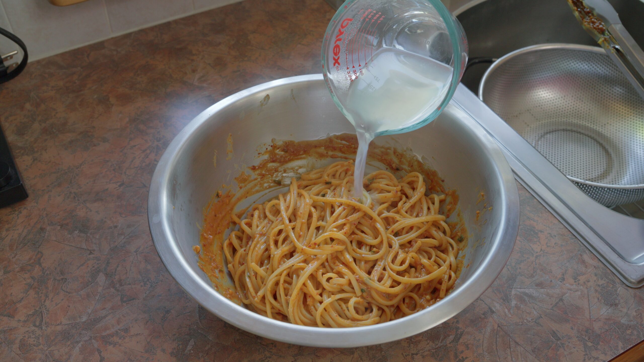 adding pasta water to thin sauce mixed with noodles