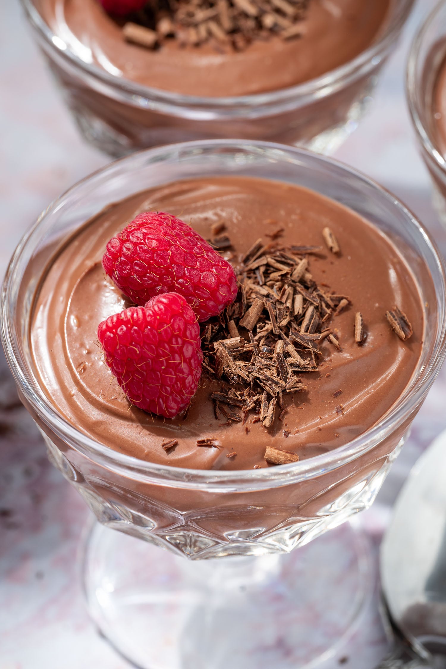 closeup of a serving of vegan chocolate mousse garnished with raspberries and chocolate shavings