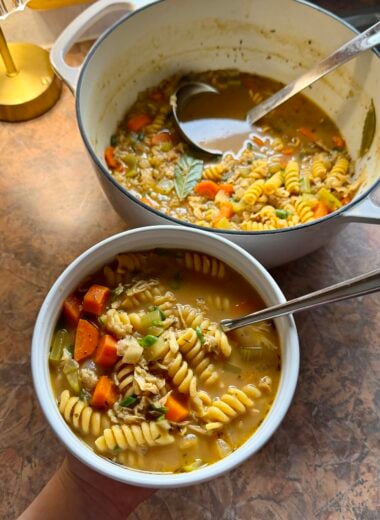 a bowl of vegan chicken noodle soup with the full pot of soup in the background